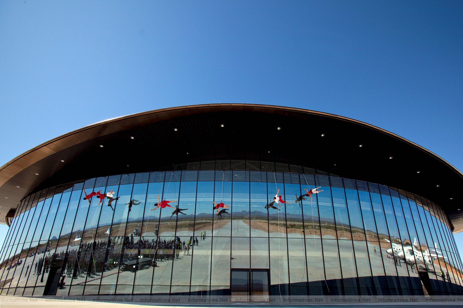 Project Bandaloop dancers based in San Francisco hang and dance on the side window wall of the Virgin Galactic Gateway to Space Hangar, Monday October 17, 2011 near Las Cruces, New Mexico..It was part of a dedication and christening of the hangar to Virgin Galactic.  Gathered crowds reflect at left and the WhiteKnightTwo with SpaceShipTwo at right. The spaceport runway tarmac reflects thoughout.