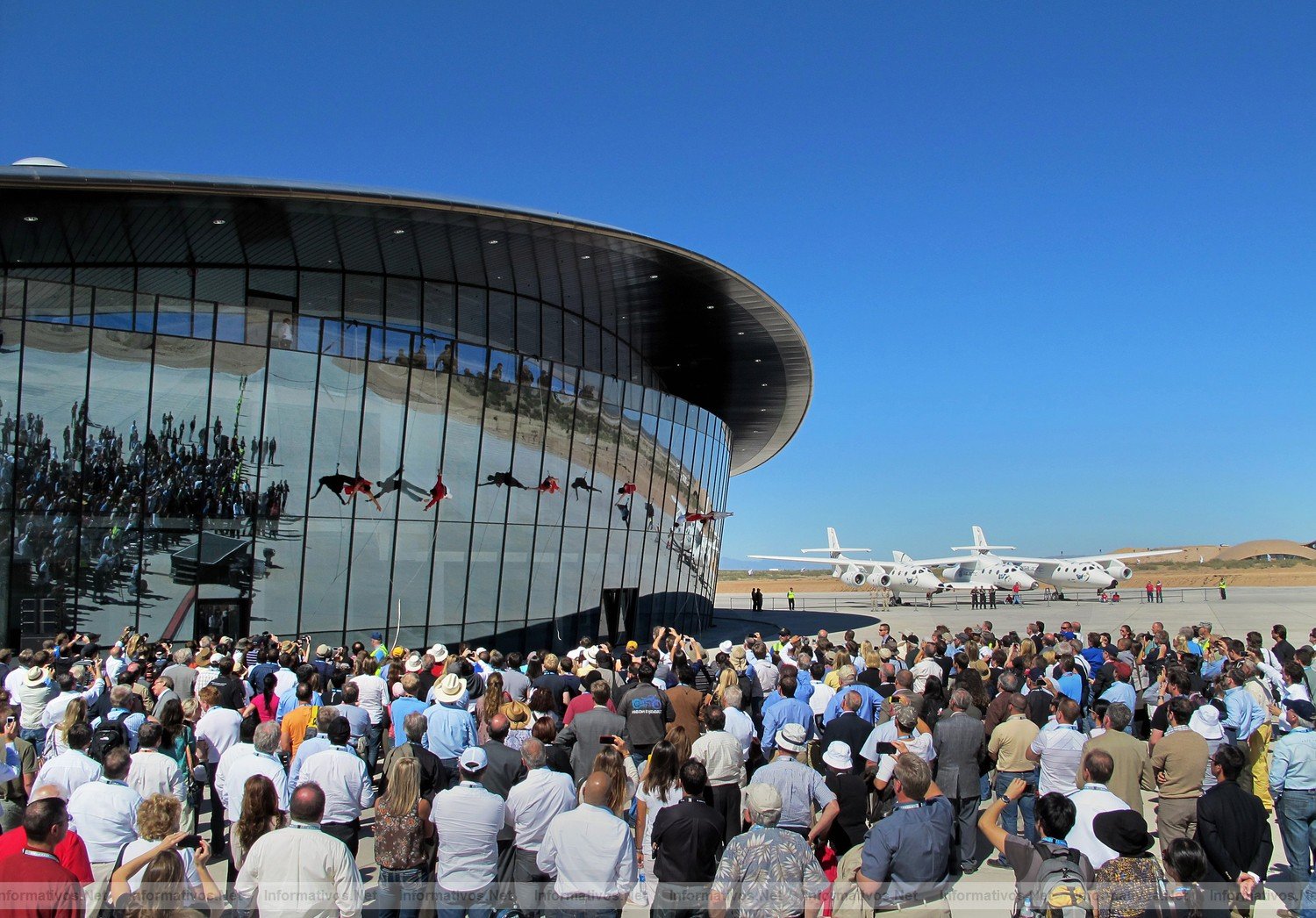 Project Bandaloop dancers based in San Francisco hang and dance on the side window wall of the Virgin Galactic Gateway to Space Hangar, Monday October 17, 2011 near Las Cruces, New Mexico..It was part of a dedication and christening of the hangar to Virgin Galactic.  Gathered crowds reflect at left and the WhiteKnightTwo with SpaceShipTwo at right. The spaceport runway tarmac reflects thoughout.
