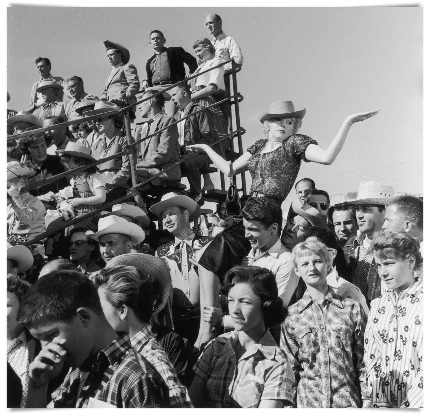 1956:  EXCLUSIVE American actor Marilyn Monroe (1926 - 1962) reacts while American actor Don Murray carries her on his shoulder on the set of director Joshua Logan's film, 'Bus Stop'. They are surrounded by a crowd in bleachers. Monroe is wearing a cowboy hat, a blouse and a slit skirt.  (Photo by Hulton Archive/Getty Images)