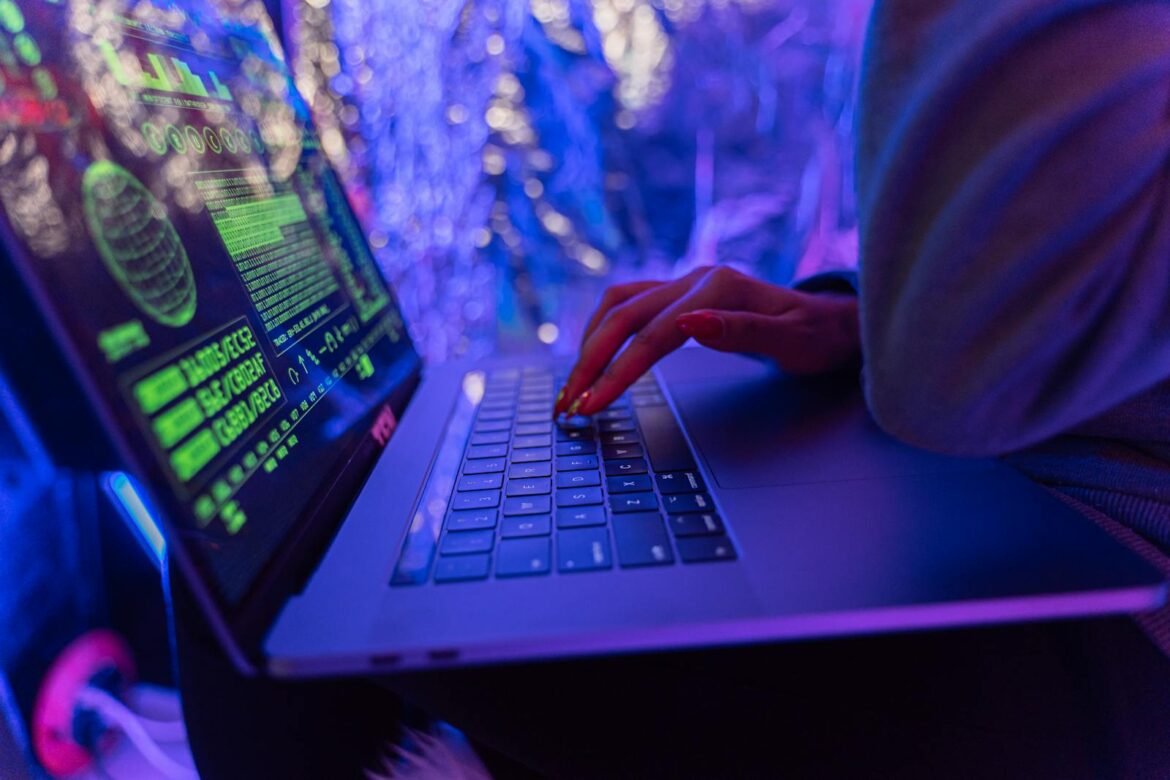 Photo by Antoni Shkraba Studio Close-up of hands typing on a laptop displaying cybersecurity graphics, illuminated by purple light.