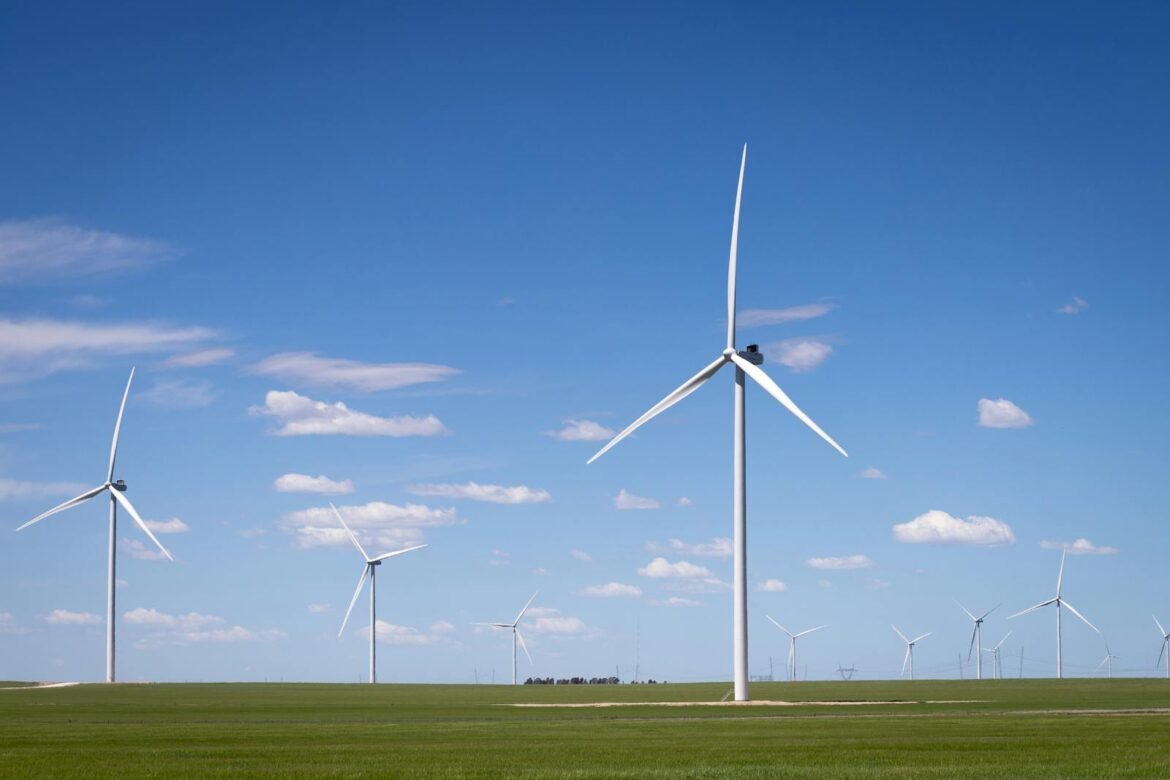 Wind turbines on green fields against a bright blue sky, highlighting renewable energy.
