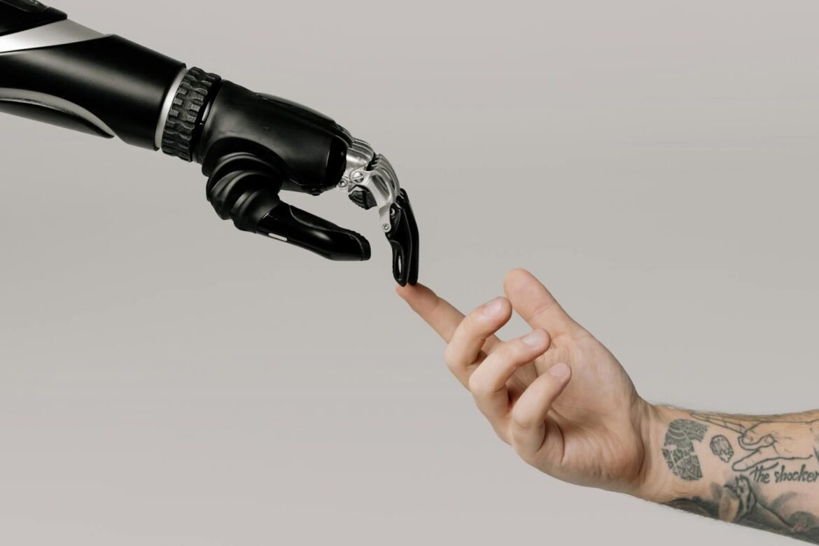 Photo by cottonbro studio A human hand with tattoos reaching out to a robotic hand on a white background.