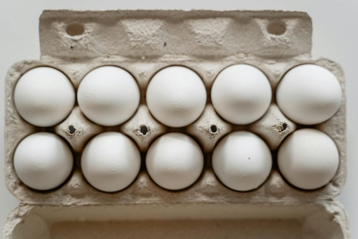 A dozen white eggs neatly arranged in a cardboard carton, viewed from above.