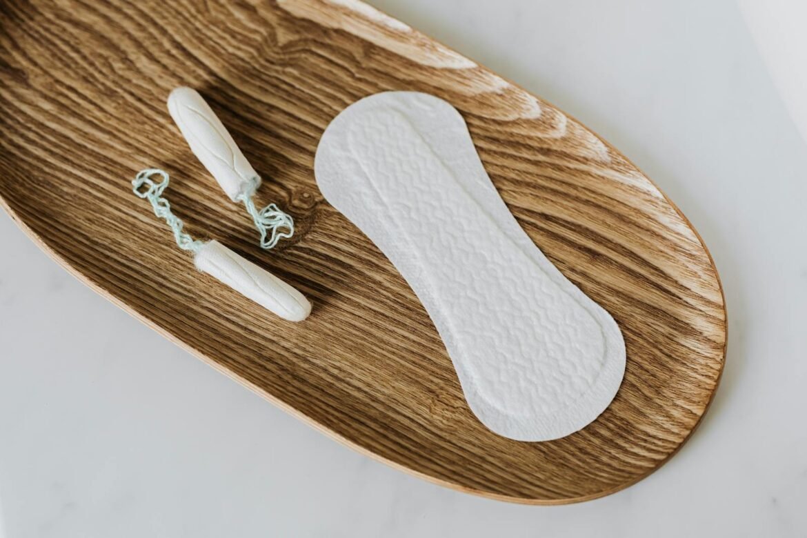 Flat lay of tampons and pad on wooden tray illustrating feminine hygiene.
