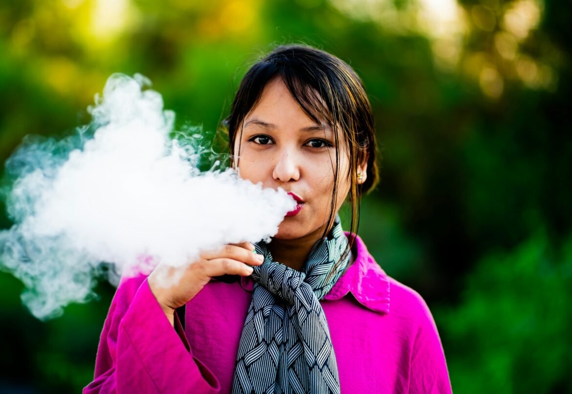 A woman in a pink shirt blowing a cloud of smoke