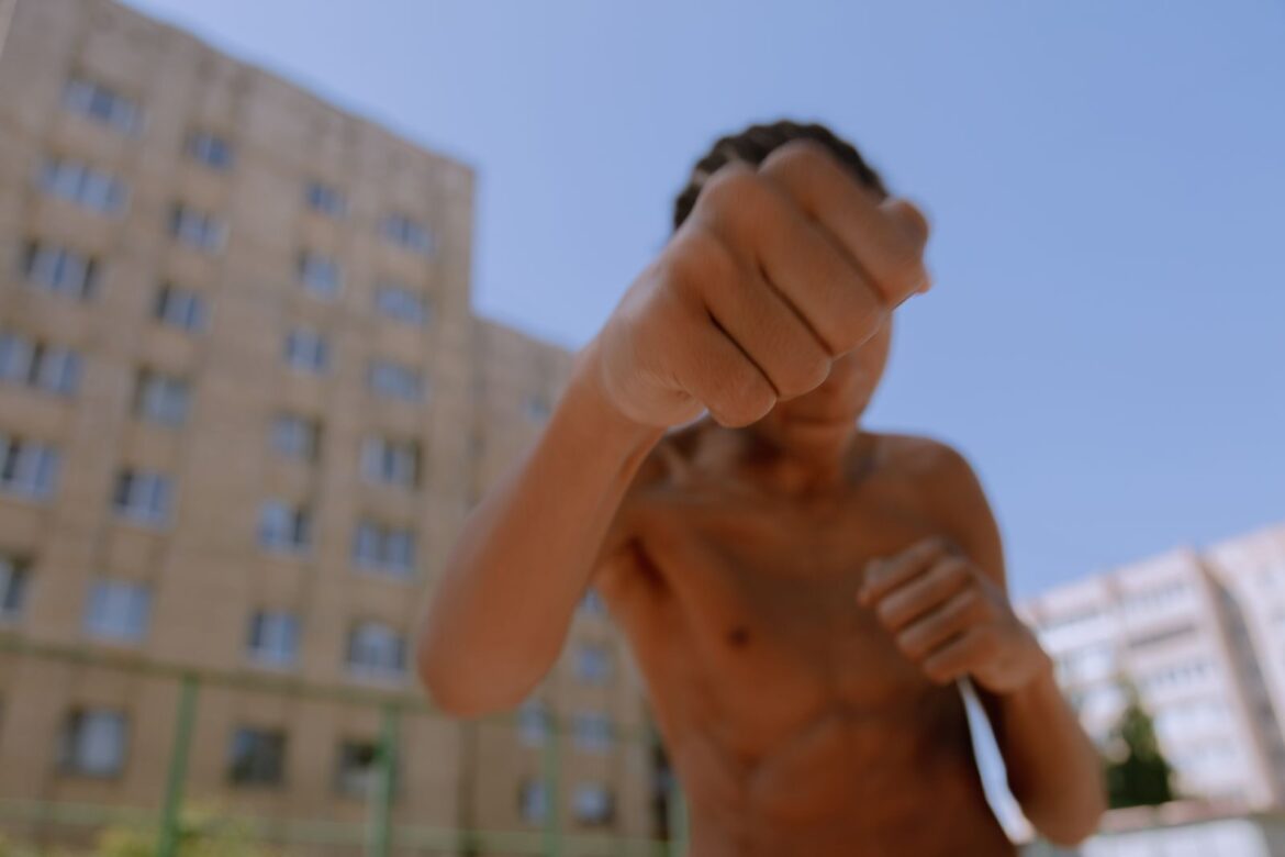 Teenager throwing a punch outside with urban buildings in the background.