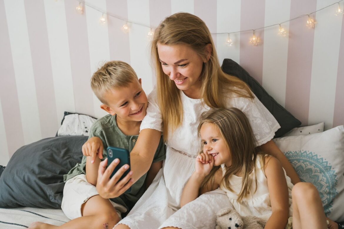 Mother and children enjoying a happy moment, sharing smiles while looking at a smartphone indoors.