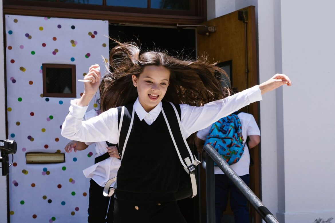 Energetic schoolgirl with backpack celebrates leaving school for the day.