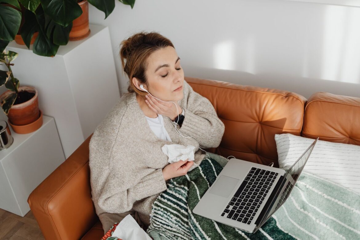 Woman relaxing with earphones on a cozy couch. Indoor scene with laptop and plants.